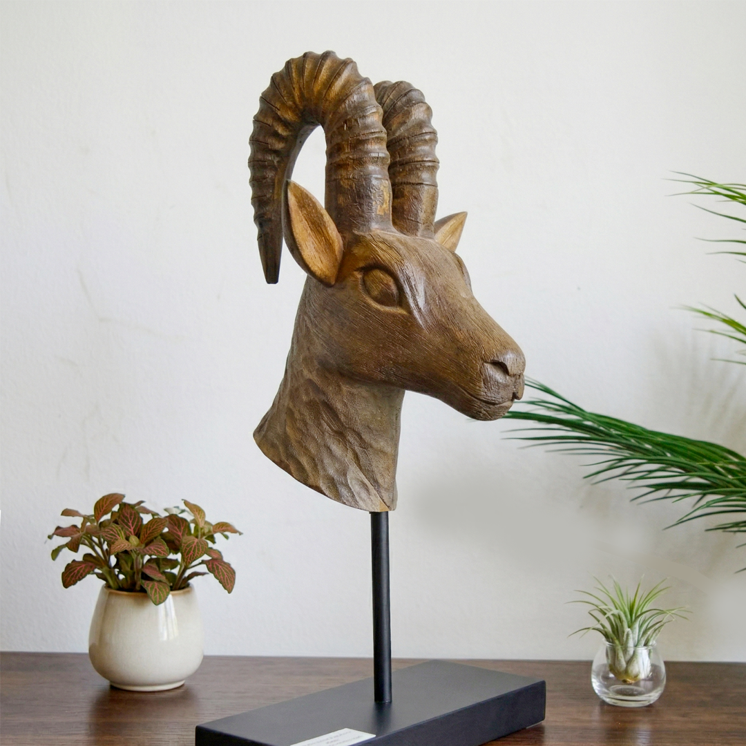 Wooden dear head sculpture on a stand with plants in the background