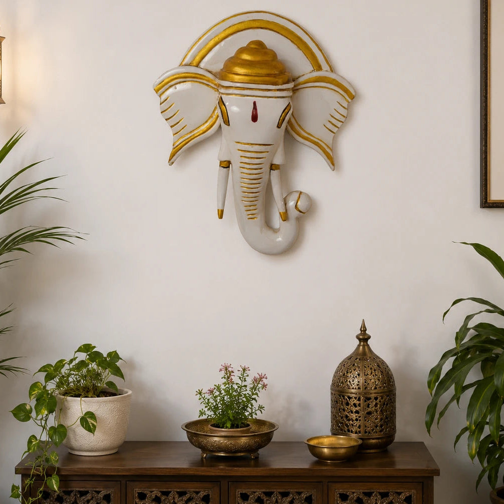 Decorative wall sculpture of an elephant head with gold accents on a white wall, above a wooden console table with decorative items.