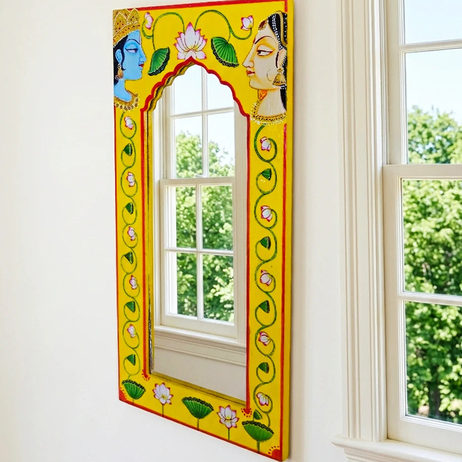 Decorative mirror with colorful frame leaning against a wall near a window.