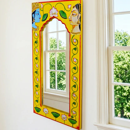 Decorative mirror with colorful frame leaning against a wall near a window.